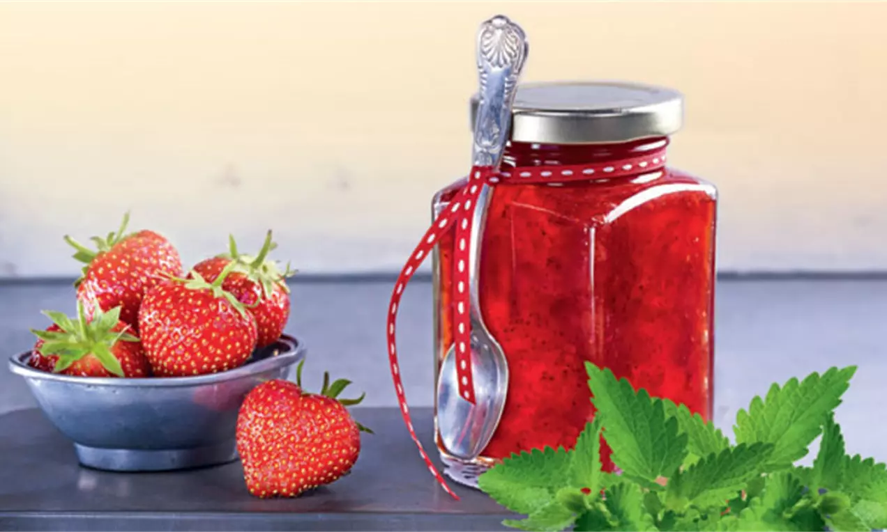 Pot de confiture rouge éclatante avec un ruban décoratif, entouré de feuilles de menthe et de fraises dans une coupe métallique