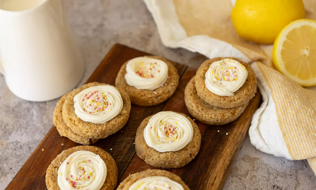 Cookies dorés à base moelleuse garnis de crème citron blanche avec éclats colorés, disposés sur une planche en bois brun