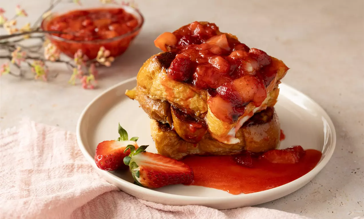 Tranches épaisses de pain doré empilées, nappées de compote rouge brillante aux fraises, sur une assiette avec des fraises fraîches