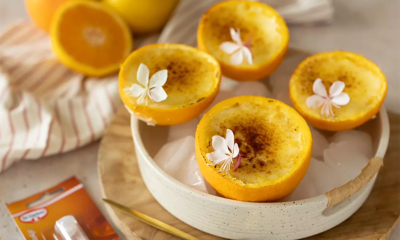 Moitiés d’oranges caramélisées garnies de crème dorée et décorées de fleurs blanches, présentées dans un bol en céramique