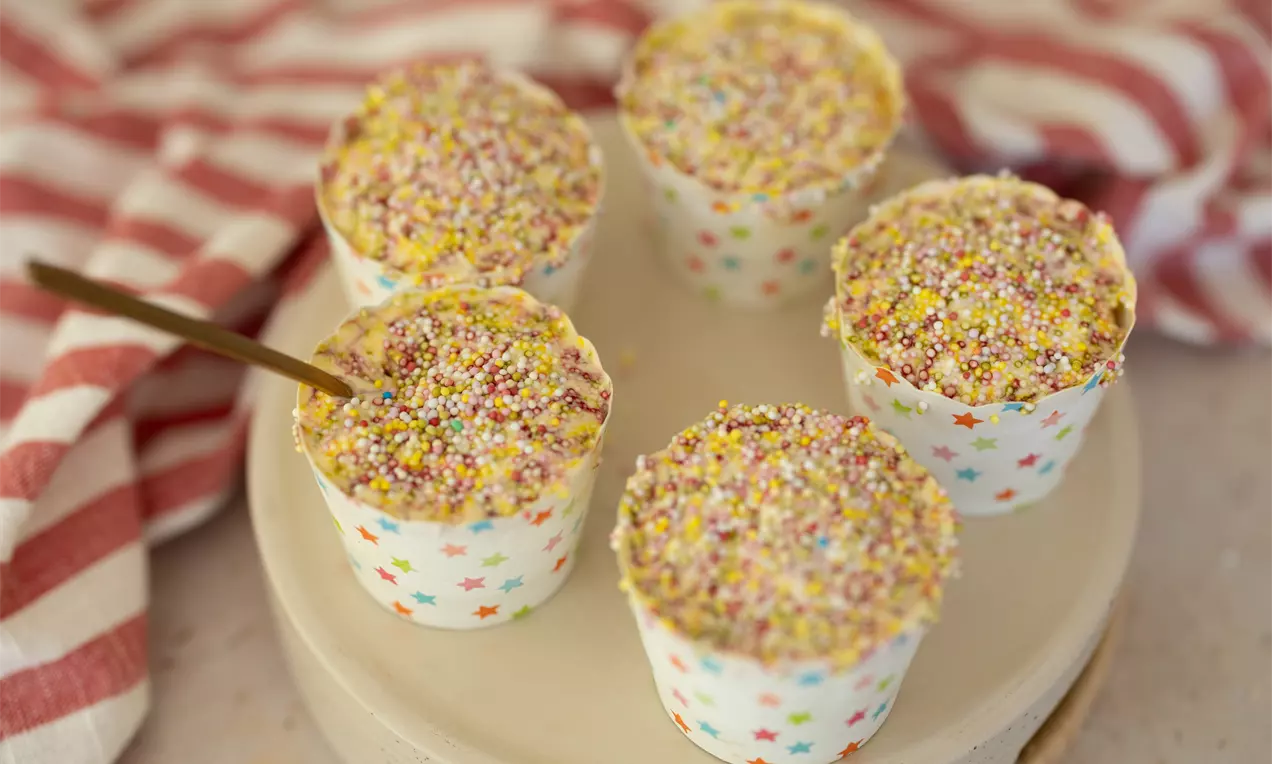 Petits desserts dans des moules blancs ornés d’étoiles colorées, garnis de billes multicolores et présentés sur un plat clair