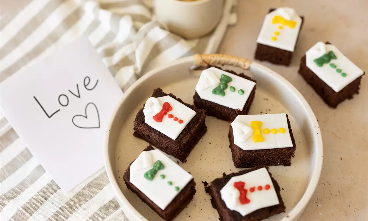 Carrés de gâteau au chocolat moelleux garnis de glaçage blanc décoré de motifs colorés sur une assiette blanche avec un café