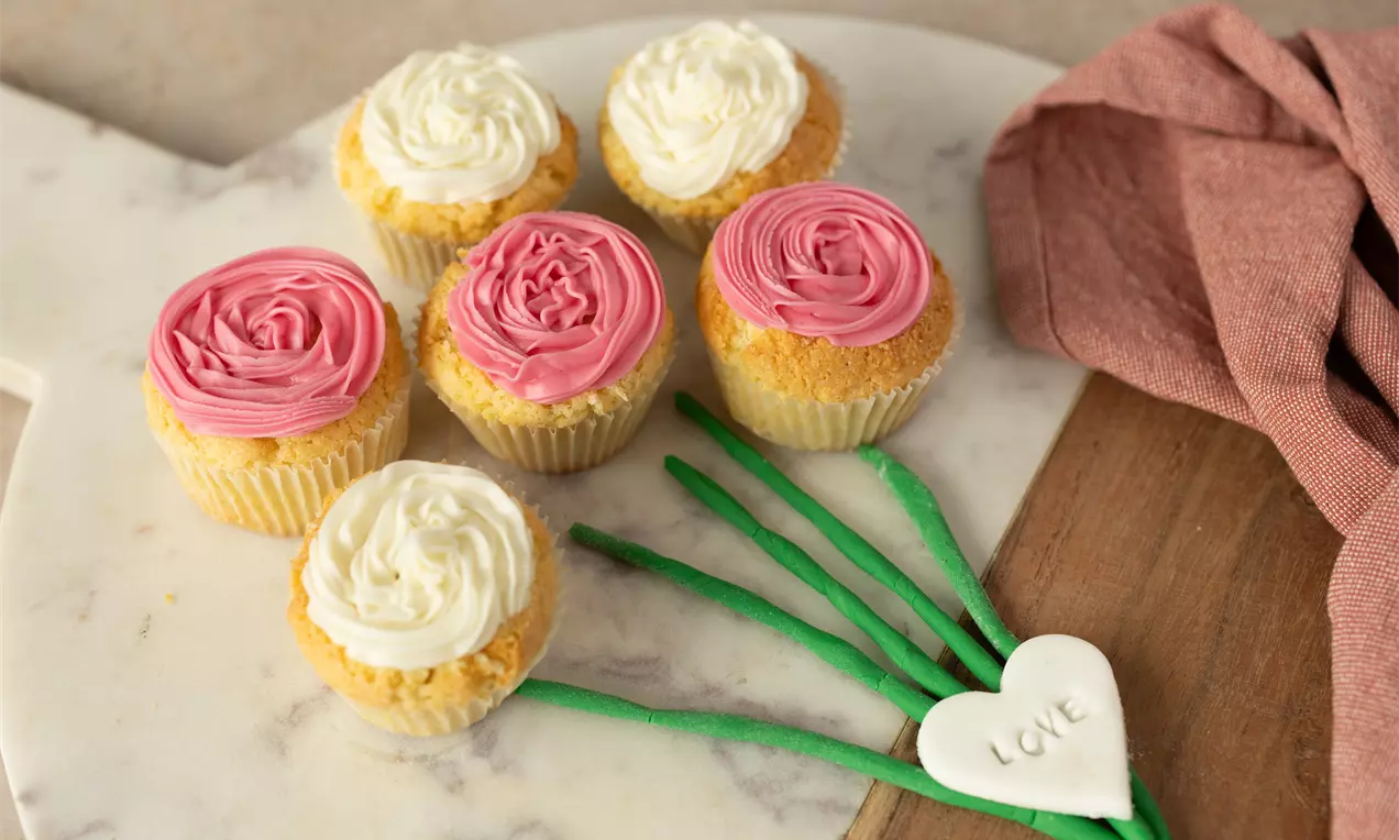 Cupcakes met zachte cakebodem, roze en witte rozetcrème, gepresenteerd op een marmeren ondergrond naast een decoratief hartje en stoffen servet