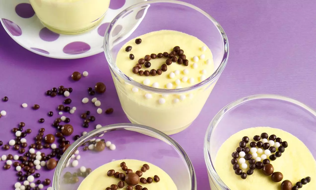 Crémeuse glace à la vanille pâle dans des verrines transparentes, décorée de billes chocolatées marron, blanches et violettes sur fond lilas
