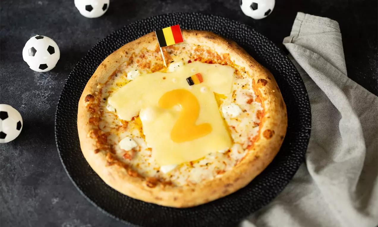 Ronde pizza met goudbruine korst, witte kaasvulling en geel kaasplaatje in de vorm van een shirt, versierd met Belgisch vlaggetje