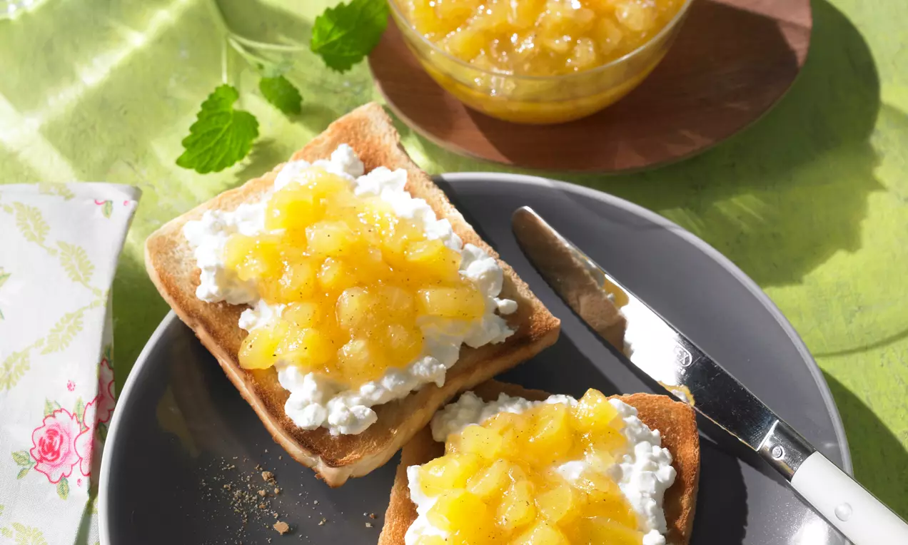 Confiture d'ananas jaune doré parsemée de graines de vanille sur deux tranches de pain grillé avec fromage frais, servie sur une assiette grise