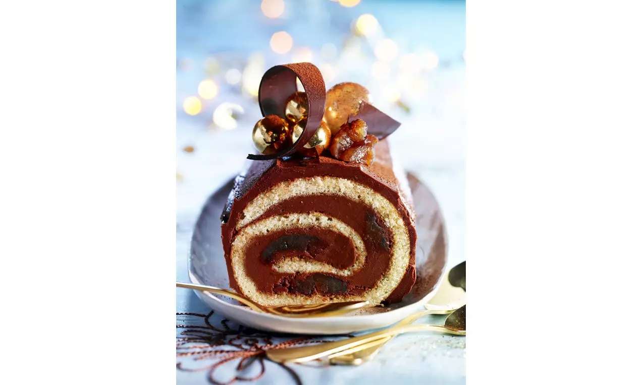 Bûche roulée chocolat et crème de marron, en spirale bicolore, garnie de volutes et éclats dorés sur une assiette blanche