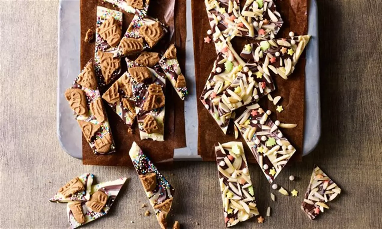 Morceaux irréguliers de chocolat marbré brun et blanc ornés de biscuits bruns, amandes effilées, éclats colorés et étoiles en sucre